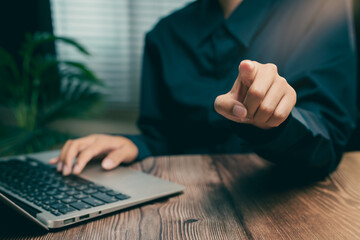 Close-up of Person Pointing at Camera with Laptop on Wooden Table in Workspace Environment, Business concept