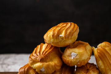 French eclair with custard. Profiteroles with cream on a white plate. Side view. Homemade pastries with cream. Dark background. Profiteroles with coffee.