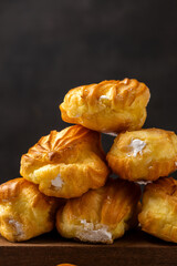 French eclair with custard. Profiteroles with cream on a white plate. Side view. Homemade pastries with cream. Dark background. Profiteroles with coffee.