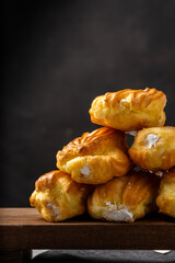 French eclair with custard. Profiteroles with cream on a white plate. Side view. Homemade pastries with cream. Dark background. Profiteroles with coffee.