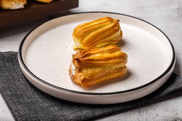 French eclair with custard. Profiteroles with cream on a white plate. Side view. Homemade pastries with cream.