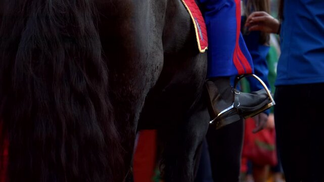 Italy, Ivrea, 03-02-2025. The foot detail of a rider in a stirrup while straddling a horse on a saddle. Slow motion 4K