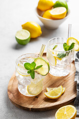 Fototapeta premium Cocktail or lemonade mojito with fresh lemon, lime, mint and ice on a wooden plate on a light background