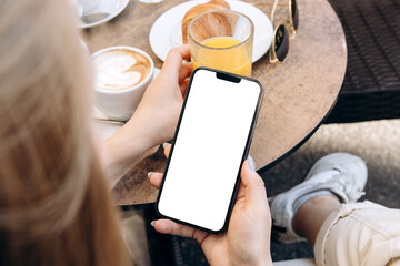 Mockup woman's hand holding using smart phone with white blank screen POV at coffee shop, mobile...