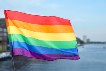 LGBT flag fluttering in city near river, selective focus
