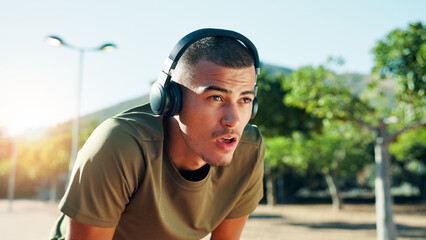 Runner, tired and man with headphones at park for workout playlist, running fatigue or breathing break. Fitness, athlete or exhausted in nature with exercise music, resting or cardio recovery outdoor