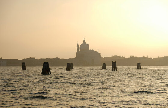 Misty sunset  or sunrise over Venetian lagoon with silhouette of historic church. Warm golden light creates dreamy atmosphere. Tranquility and beauty of Venice, historical landscape.