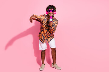 Trendy young man singing karaoke with microphone and colorful glasses on pink background...
