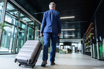 Man in elegant suit carrying a big suitcase and going to the airport exit