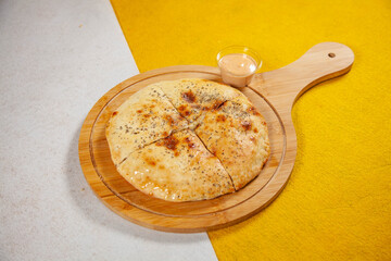 Rounded flatbread stuffed naan served on a wooden plate with side dip on a white and yellow diagonal background Mediterranean food.