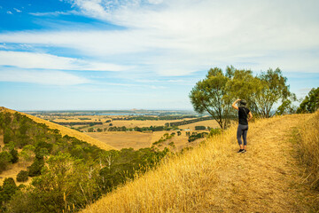 Fototapeta premium Rear view of woman standing on walking trail in a hill, overlooking the view in the far distance, Mount Sugarloaf, Camperdown, Victoria, Australia