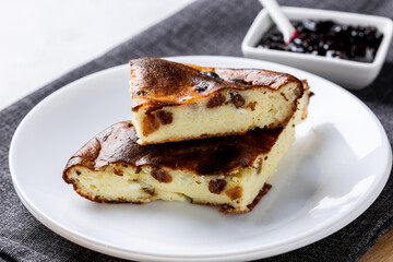 Cottage cheese casserole with berry jam on a white plate. Homemade casserole with cottage cheese and raisins.