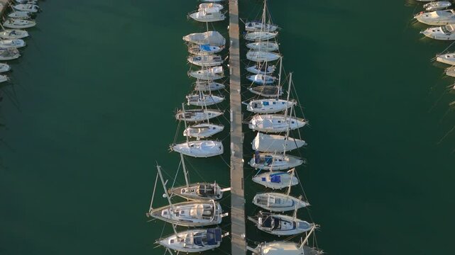 A beautiful aerial video capturing a symmetrical view of sailboats neatly docked along both sides of a central pier in a tranquil marina. 