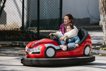 Happy and excited Chinese  woman and her cute little daughter driving bumper car in the amusement park. Happy people concept.