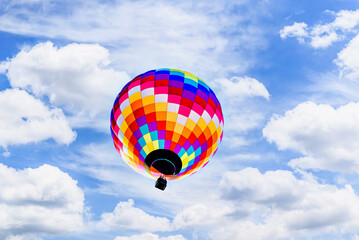 Colorful hot air balloon flying over blue sky with white clouds