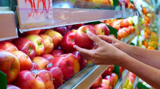 Shopper selecting ripe apple in supermarket focusing on quality and freshness Apple symbolizes healthy food choice Careful apple selection highlights importance of nutritious and mindful shopping