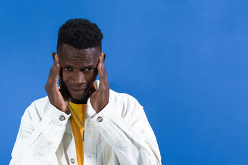 Young man suffering from headache touching temples on blue background
