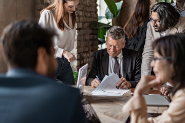 Senior businessman signing contract at team meeting in modern office