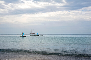 Beautiful picturesque view of the seashore and skyline at sunset. Sailboat and some pedalos moored in front of the beach with the horizon behind. 