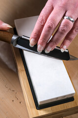 A close-up of a person sharpening a knife on a whetstone. The hands guide the blade at the correct...