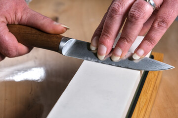 A close-up of a person sharpening a knife on a whetstone. The hands guide the blade at the correct...