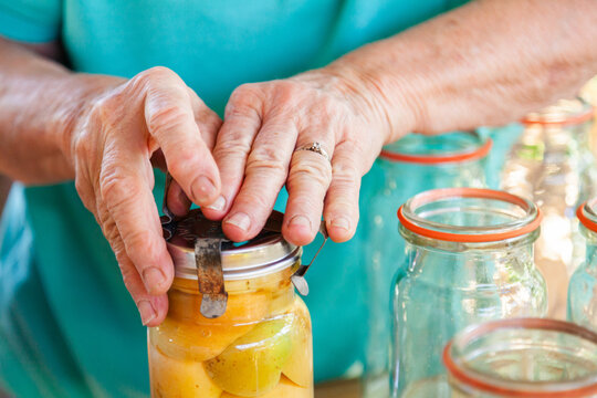 Person putting lid on jar with canned fruit inside