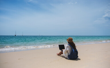 A female traveler using and working on laptop computer while sitting on the beach