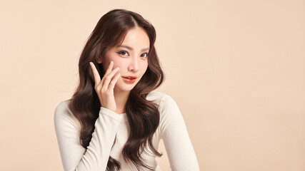 Fototapeta premium A beautiful young Asian woman with clean, fresh skin against a beige background. Skincare, facial treatment, cosmetology, beauty, and spa. An elegant portrait of an Asian woman.