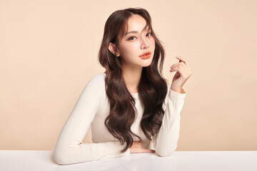 Fototapeta premium A beautiful young Asian woman with clean, fresh skin against a beige background. Skincare, facial treatment, cosmetology, beauty, and spa. An elegant portrait of an Asian woman.