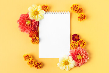 Open paper notebook with empty page for your text and flowers pink dahlias and marigolds on a yellow background. Nature trendy decorative design. Flat lay.