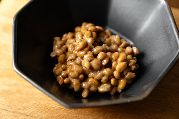 ネバネバの糸を引いている納豆　黒いボウル　木製テーブルの背景