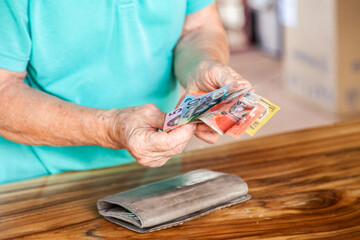 Old persons hands handing over australian bank notes