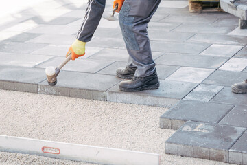 A worker installs concrete paving slabs using a rubber mallet and gloves. Precise leveling ensures...