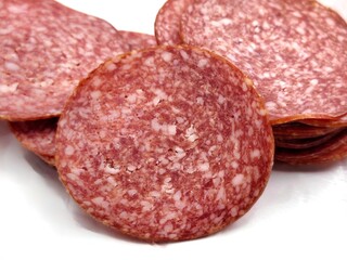 Closeup view of sliced spicy air-dried salami with a marbled texture, isolated on white background, showcasing its rich red color and white fat specks.
