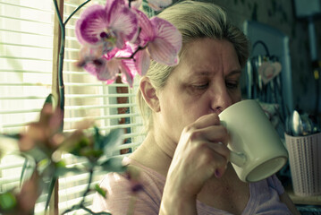 A woman is drinking coffee while looking at a plant