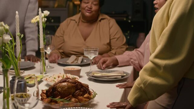 Close up on hands of Black woman serving roasted turkey as main course then senior lady and guests making compliments to aromatic dish during festive dinner at home, rack focus