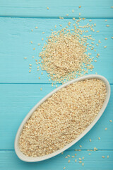 Raw sesame seeds in white bowl on blue background. Vertical photo