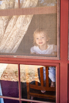 cheeky little boy on chair looking out gauze window