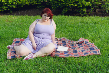 Young plus-size woman sitting posing in the park calmly looking at the camera