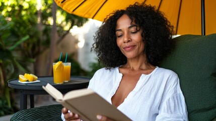 A woman sits outside reading a book while enjoying a drink and holding an umbrella, with fruit around her, on a sunny day.