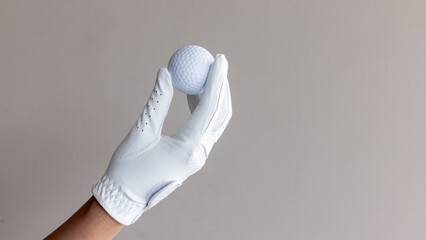 Woman hand wear white golf glove hold white golf ball, Player golfer woman hold golf ball on beig...