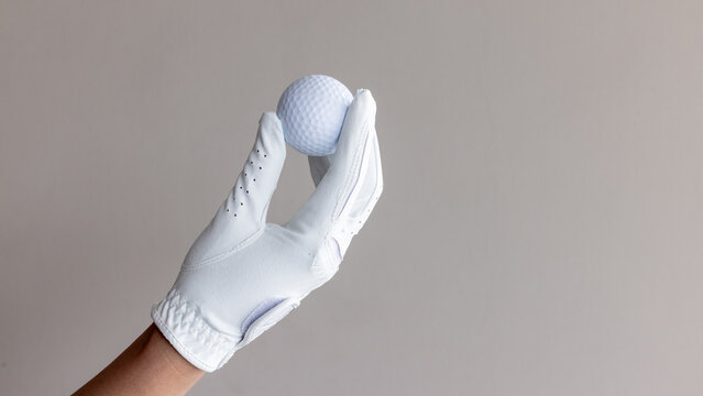 Woman hand wear white golf glove hold white golf ball, Player golfer woman hold golf ball on beig background, Hand wearing golf glove holding white golf ball, Love golf concept.