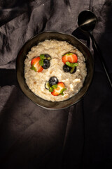 Oatmeal porridge with strawberries and blueberries and chia seeds on a black background