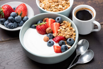 Granola bowl with yogurt, berries and served with a cup of espresso coffee, wooden table background