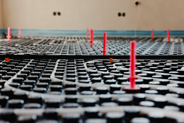 Underfloor heating system installation showing white plastic pipes and mounting studs being laid on...