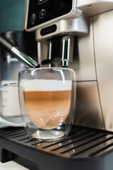 Home coffee maker pouring cappuccino into glass mug in kitchen
