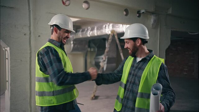 Two happy Caucasian men greeting friends buddies males guys workers in uniform helmets business construction teamwork engineers architects meeting shaking hands building cooperation colleagues gesture