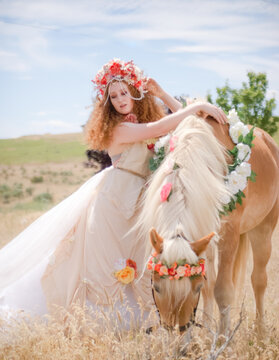 portrait of a red haired woman with flower crown wearing a long flow dress leaning against Halfinger horse with flowers in mane