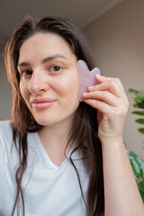 Woman performs a gua sha face massage to reduce morning puffiness and lift the facial contour with...