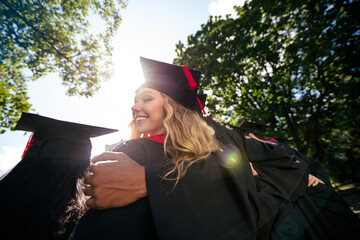 Rear photo of company groupmates students smile embrace mortarboard gown graduate college outdoors